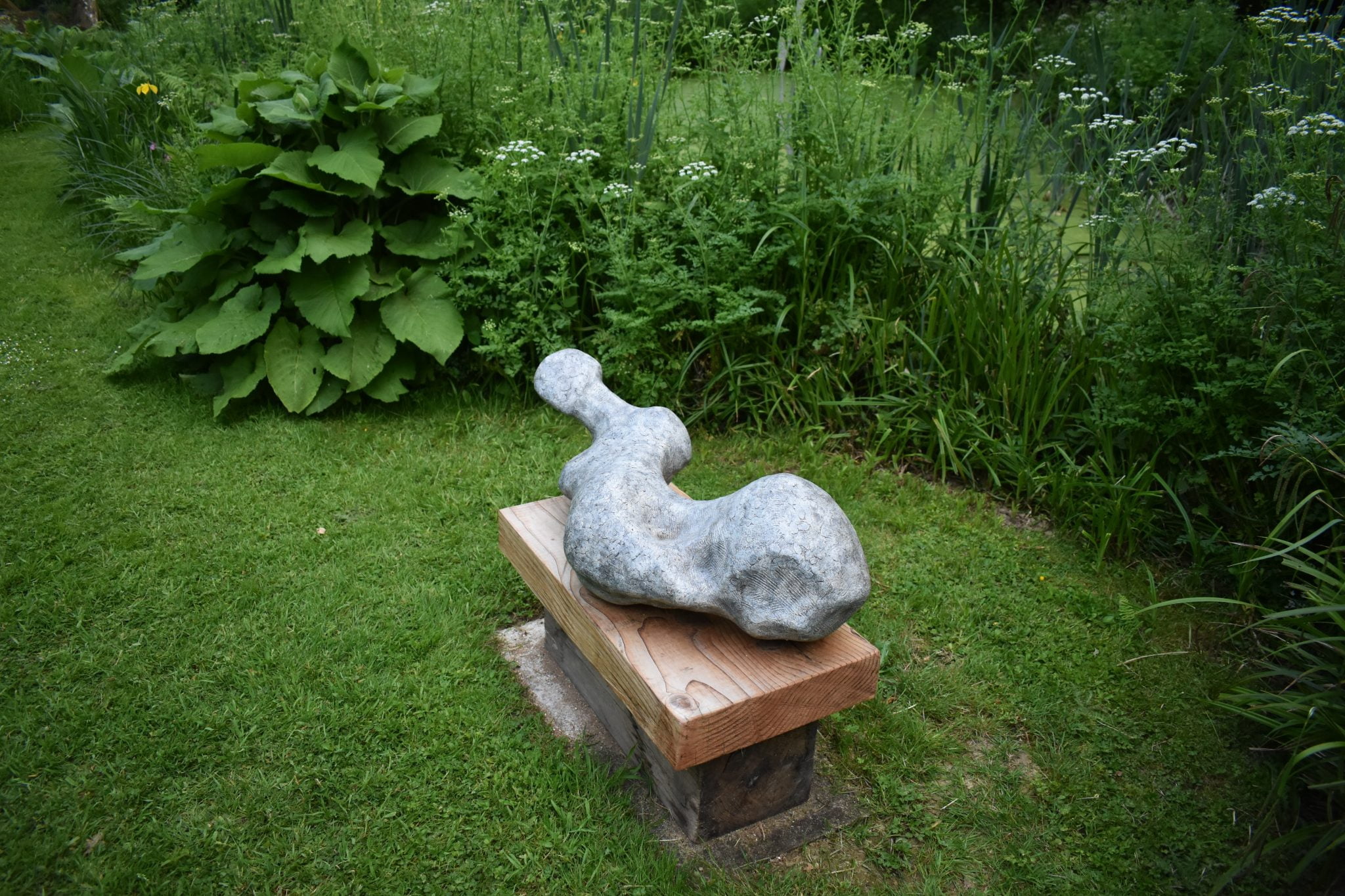 An abstract sculpture of a female figure placed in a garden setting