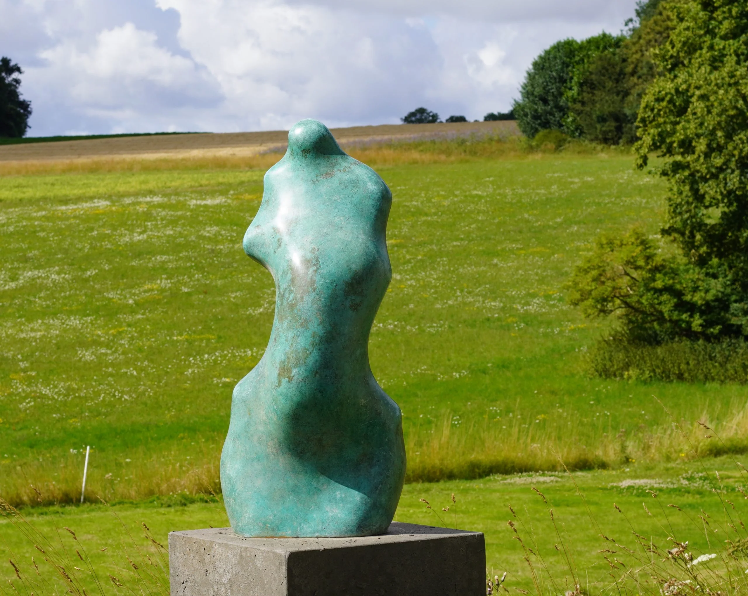 Female torso sculpture situated in a garden with fields in the background