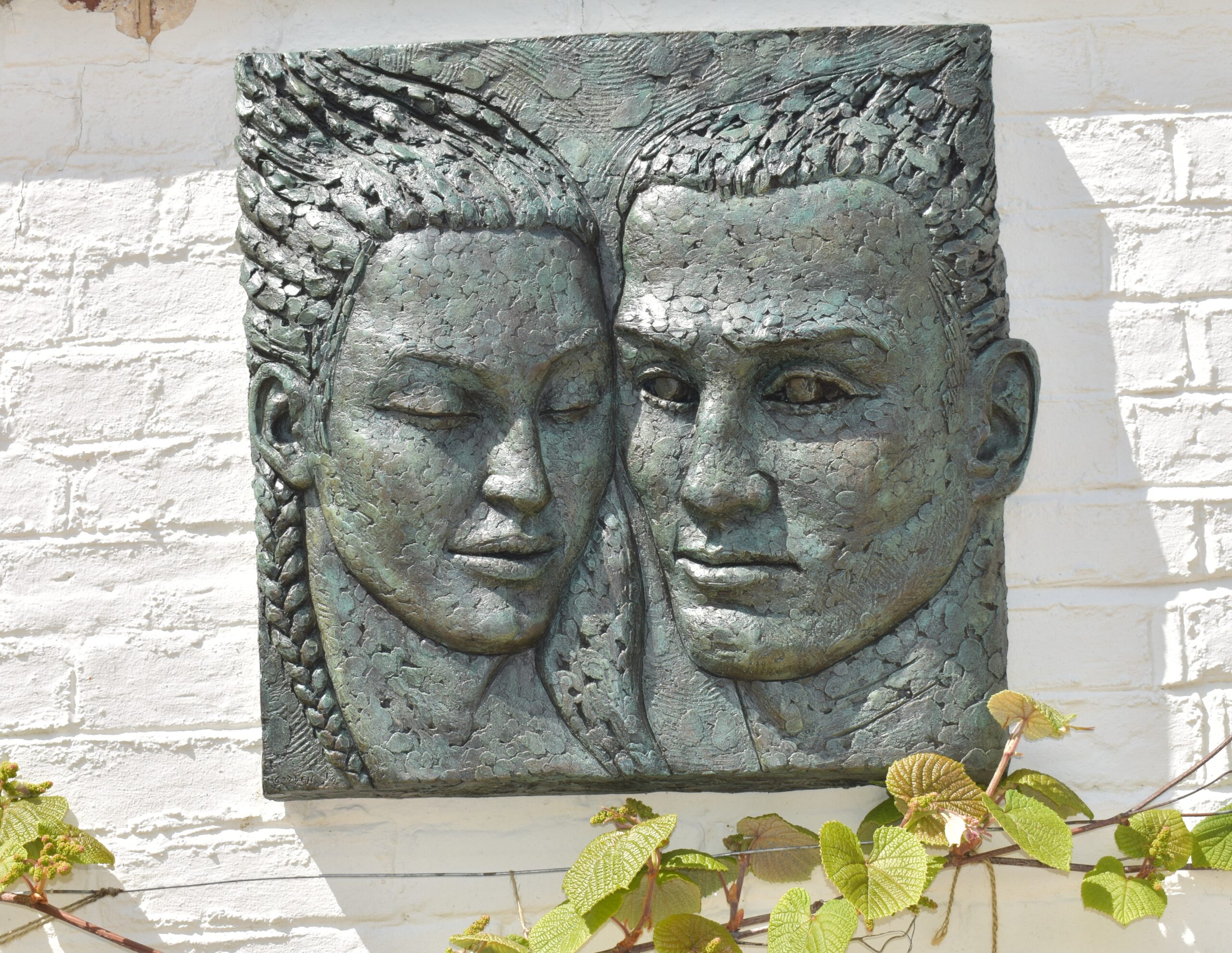 Bronze wall sculpture of two faces mounted on white brick wall